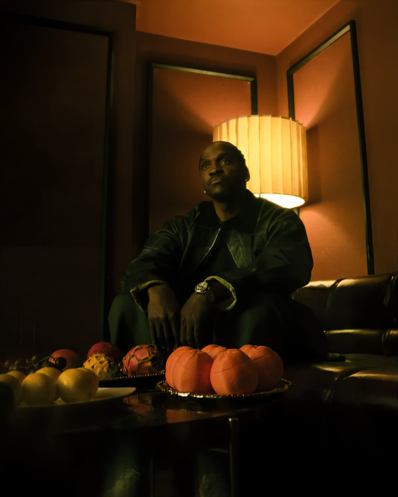 A man on a leather sectional looking up past the camera, silver trays of ceramic oranges and lemons across the foreground
