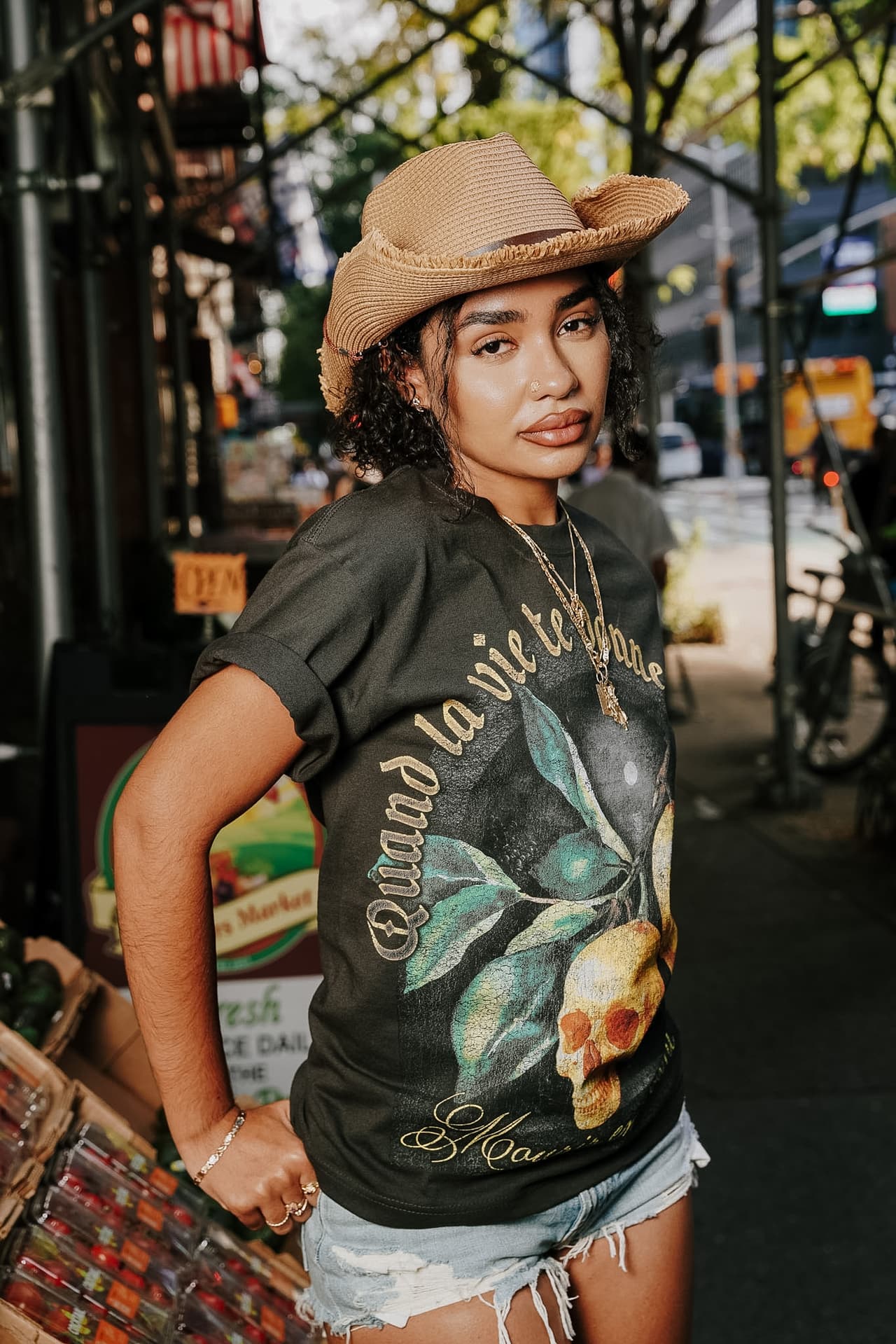 Model in the lemon-skulls tee holding a fruit basket in front of the Stiles storefront window