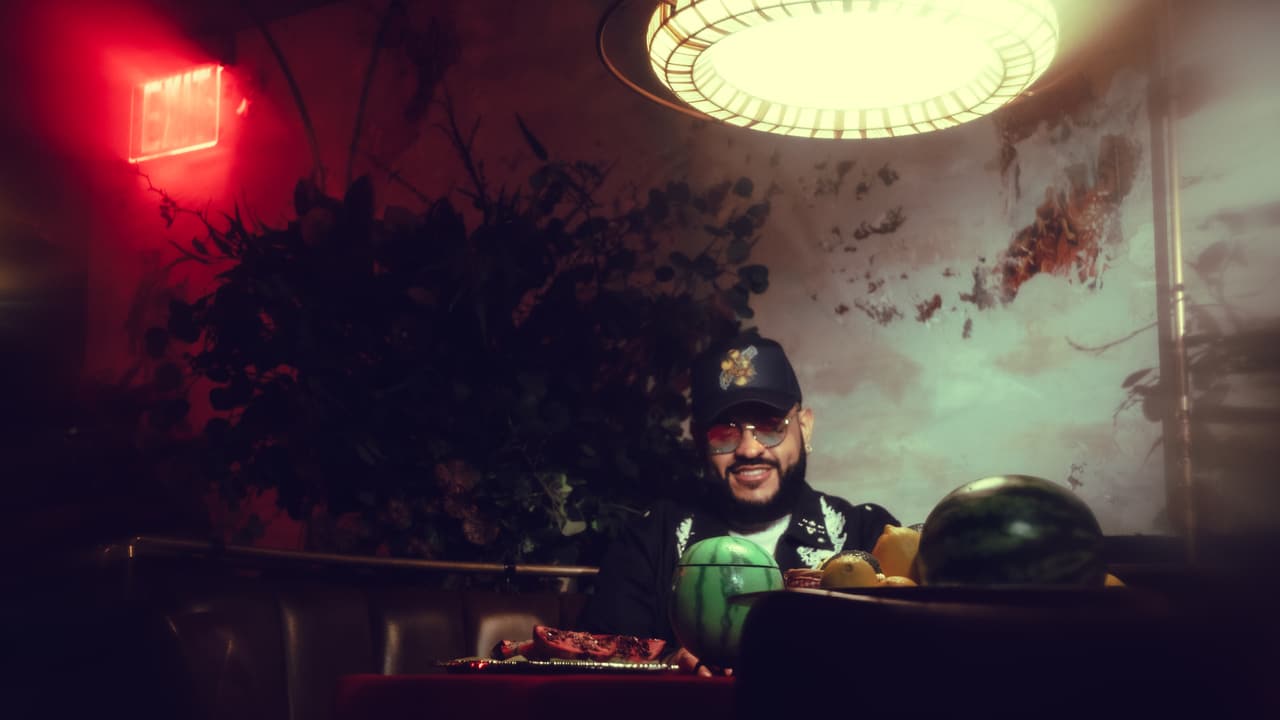 Dark bar interior with red neon and a hanging lamp over a red table, a man small at frame right