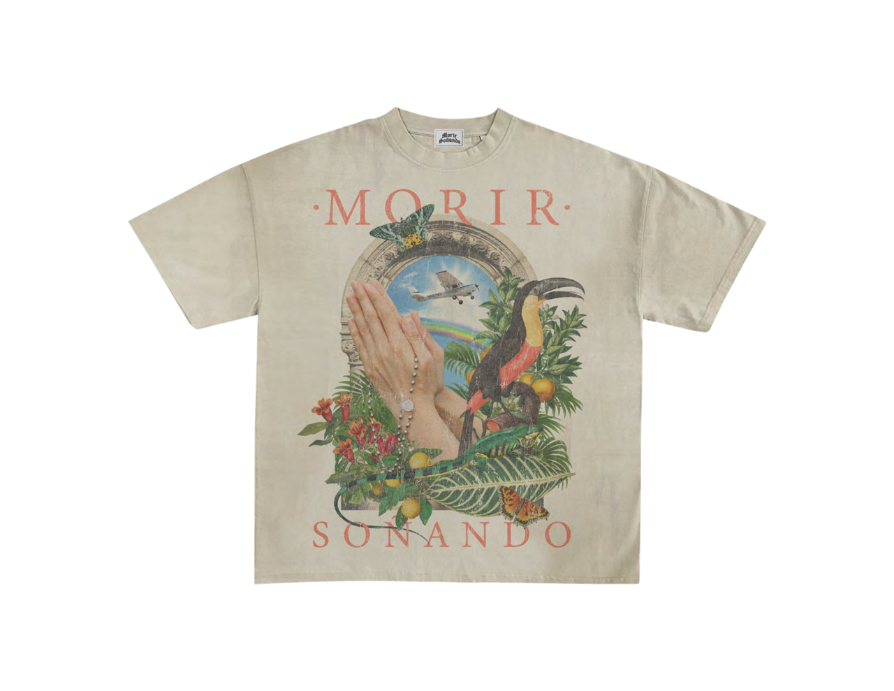 Sand t-shirt mockup with praying hands and a rosary under a stone arch, a small plane, a rainbow and a toucan among tropical leaves