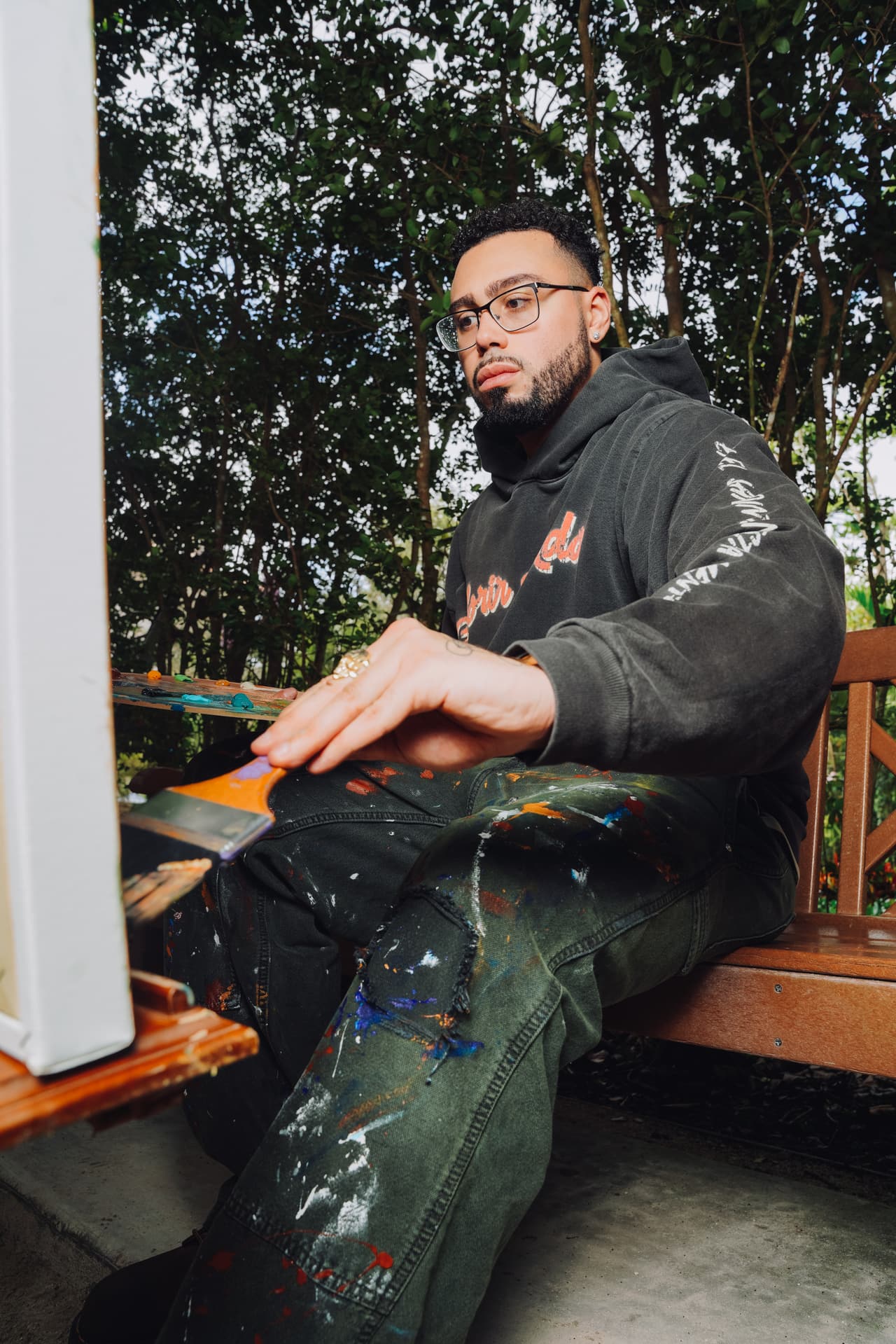 Painter seated on a garden bench in the harvest hoodie, the cream sleeve text running the length of his arm