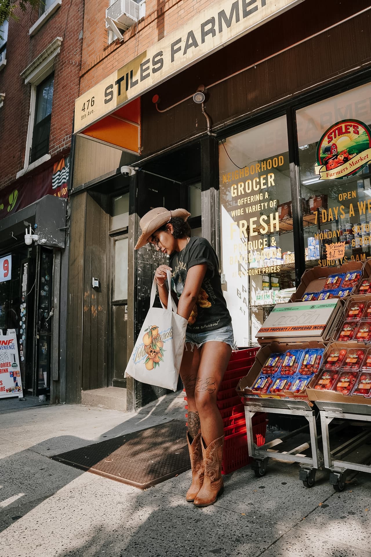 Woman carrying the canvas tote at her hip along a market awning on a bright sidewalk