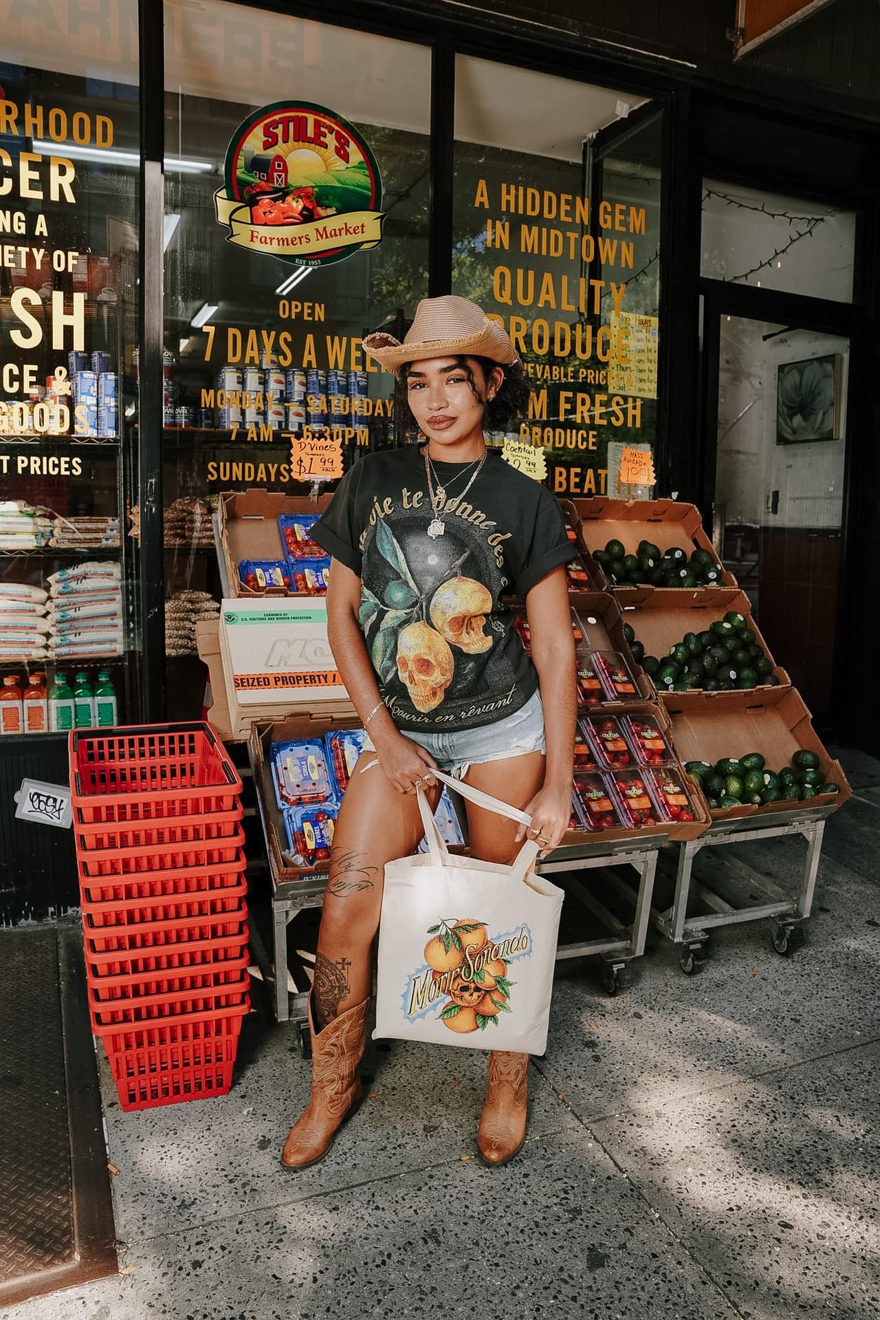 Woman in a straw hat holding the canvas tote open-handed in the doorway of a corner grocery
